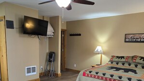 A bedroom with a bed, a ceiling fan, a TV mounted on the wall, and a lamp.