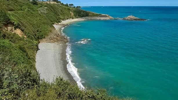 A coastal landscape with a beach, clear turquoise waters, and a rocky outcrop.