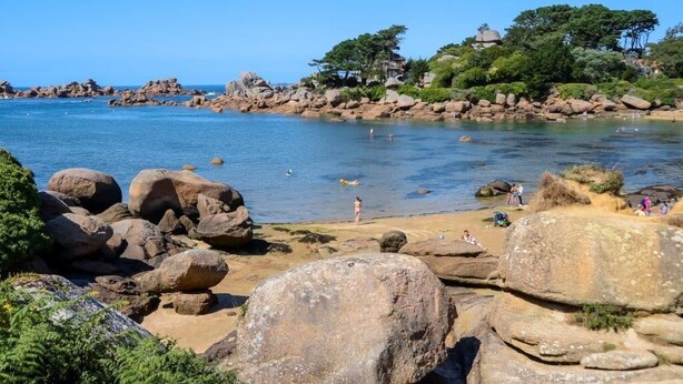 A rocky beach with large boulders, clear blue water, and a few people enjoying the area. - Les Hortensias - ST Quay Perros (ST QUAY PERROS)