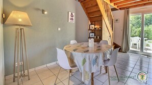 A dining area with a round table, white chairs, a floor lamp, and a staircase leading to an outdoor area with a view of greenery. - Les Hortensias - ST Quay Perros (ST QUAY PERROS)