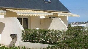 A house with a sloped roof, two windows, and a covered patio area. - Les Hortensias - ST Quay Perros (ST QUAY PERROS)