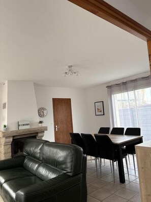 Un salon moderne avec un canapé en cuir, une table à manger, des chaises, une cheminée et une grande fenêtre.