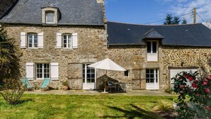 Une maison en pierre avec un patio, un petit jardin et un parasol blanc.