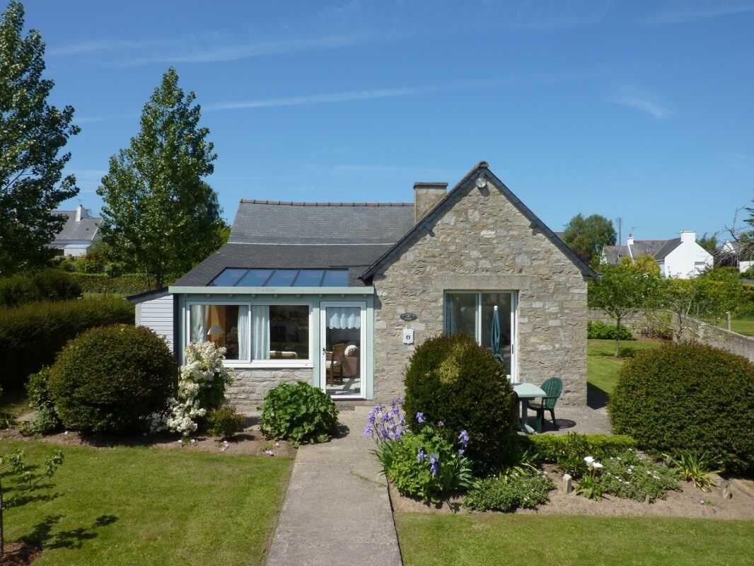A stone house with a sloped roof, a covered porch, and a garden with various plants and flowers.