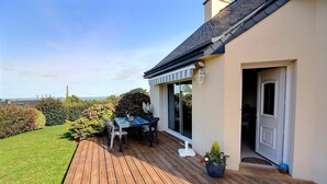 A wooden deck with a table and chairs, a potted plant, and a door leading to a room. - Ker Mignonette - Trevou Treguignec (TREVOU TREGUIGNEC)