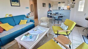 A living room with a blue sofa, yellow armchairs, and a dining area with a table and chairs. - Ker Mignonette - Trevou Treguignec (TREVOU TREGUIGNEC)