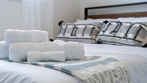A neatly made bed with rolled white towels, a blue and white striped blanket, and patterned pillows.