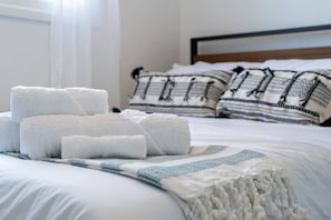 Ein ordentlich bezogenes Bett mit aufgerollten weißen Handtüchern, einer blau-weißen Streifendecke und gemusterten Kissen.