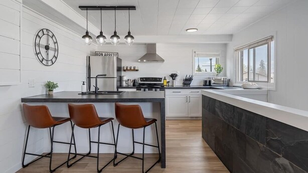 A modern kitchen with a central island, bar stools, pendant lighting, and a clock on the wall.