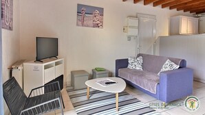 Un salon avec un canapé, un téléviseur posé sur un meuble, une petite table et une chaise.