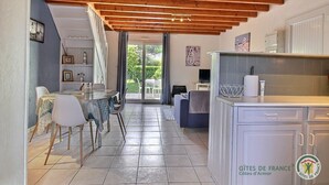 Une cuisine chaleureuse avec un sol carrelé, des poutres en bois au plafond et un coin repas comprenant des chaises et une table.