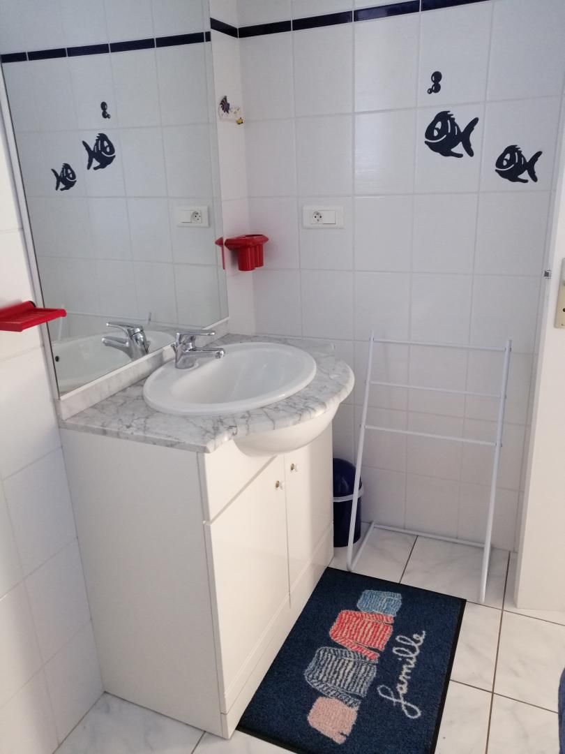 A bathroom with a white sink, mirror, and tiled walls. There are fish decals on the wall and a red soap dish.