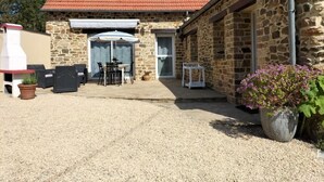 Ein Steinhaus mit rotem Ziegeldach, einer Terrasse mit Gartenmöbeln und einem Blumentopf.