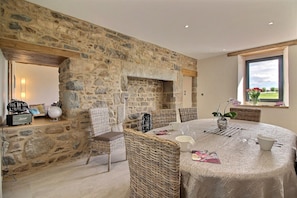 A dining area with a stone wall, wicker furniture, and a table set for four. - Sheltered by the pines - PLEUBIAN (PLEUBIAN)