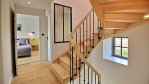 A modern staircase with wooden steps and black balusters, leading to a bedroom with a bed and a nightstand. - Sheltered by the pines - PLEUBIAN (PLEUBIAN)