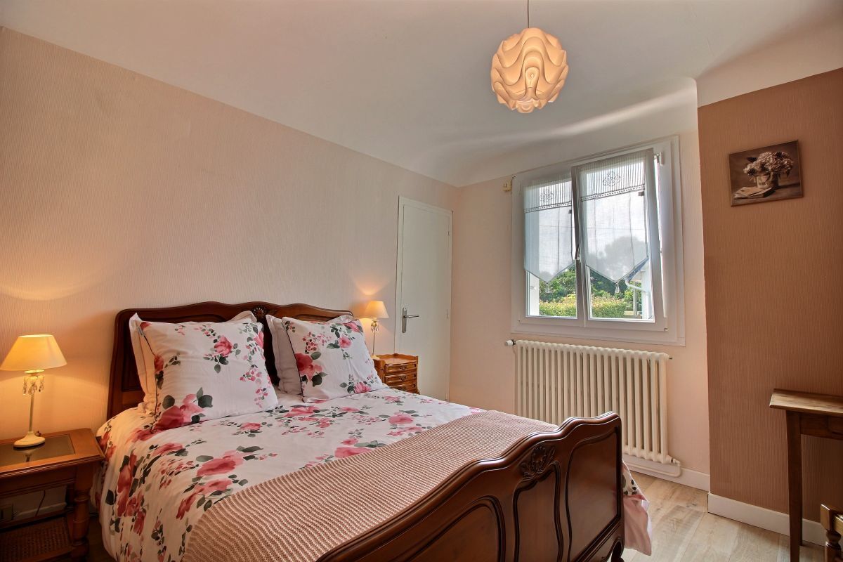 Une chambre avec un lit en bois, une table de chevet avec une lampe, une fenêtre donnant sur un paysage verdoyant et un radiateur.