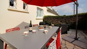 Une table à manger avec un parasol rouge, une bouteille de vin, ainsi que plusieurs bols et assiettes.