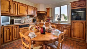Une cuisine avec des meubles en bois, une table à manger avec des chaises, une bouilloire et une fenêtre donnant sur un beau paysage.