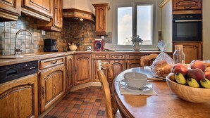 Une cuisine avec des meubles de rangement en bois, un mur recouvert de carreaux, une fenêtre et une table à manger ornée de fruits.