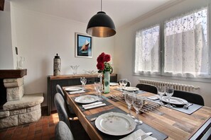 Un coin repas avec une longue table en bois dressée pour six personnes, un luminaire suspendu noir et un vase rempli de fleurs rouges.