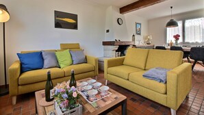 Un salon avec deux canapés jaunes, une table basse sur laquelle se trouvent une bouteille et des fleurs, et un coin repas à l’arrière-plan.
