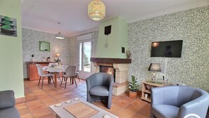 A living room with a fireplace, a dining area, and a TV mounted on the wall. - Le Jardin - Plestin LES Greves (PLESTIN LES GREVES)