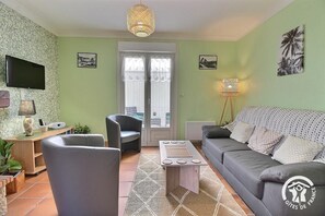 A living room with a grey sofa, two armchairs, a coffee table, a TV, and a patterned rug.