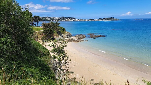 A coastal beach with clear blue water, sandy shore, and a distant town. - Le Jardin - Plestin LES Greves (PLESTIN LES GREVES)
