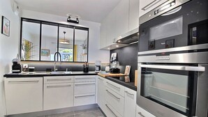 Una cocina moderna con armarios blancos, encimera negra y electrodomésticos de acero inoxidable, incluyendo un horno y una cafetera.