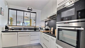 A modern kitchen with white cabinets, a black countertop, and stainless steel appliances including an oven and a coffee maker.