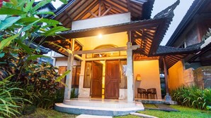 A traditional-style building with a covered entrance, a stone pathway leading to the door, and a small outdoor seating area with chairs. - Outpost Ubud Coliving Suites (Ubud)
