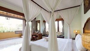 A bedroom with a four-poster bed, a desk, and a chair, with a view of greenery outside. - Outpost Ubud Coliving Suites (Ubud)