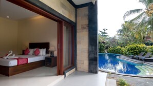 A bedroom with a large bed, a nightstand, and a window overlooking a swimming pool. - Outpost Ubud Coliving Suites (Ubud)