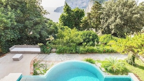 Une piscine dotée d’une terrasse en pierre, entourée d’une végétation luxuriante et offrant une vue sur la mer et les montagnes.