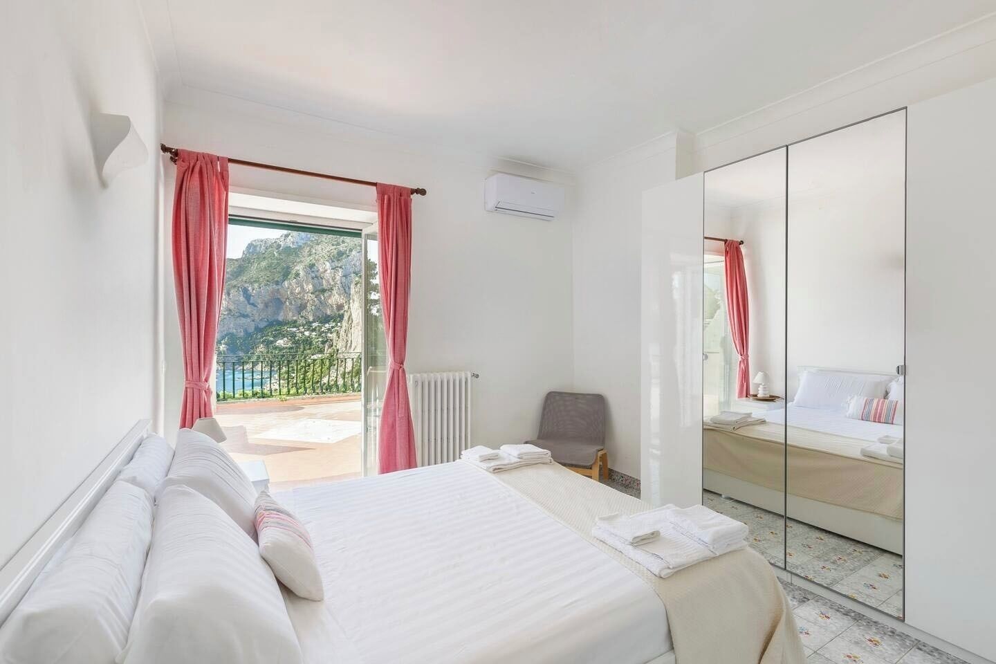 A hotel room with a bed, a chair, a large mirror, and a view of the outdoors.