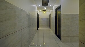 A corridor with marble walls and tiled flooring, leading to doors with a dark frame. - Treebo Trend Hotel Sampradaya (Bengaluru)