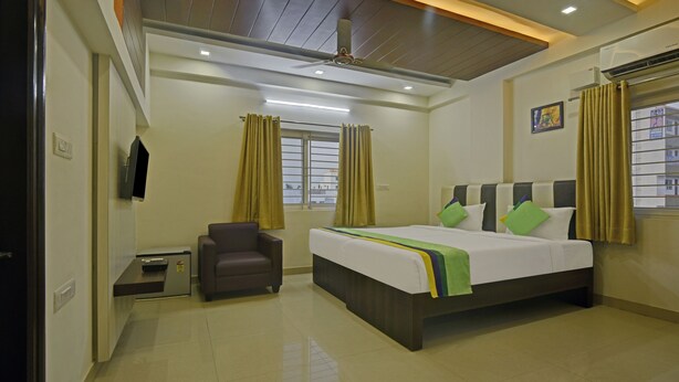 A hotel room with a bed, a chair, a TV, a window with curtains, and a ceiling fan. - Treebo Trend Hotel Sampradaya (Bengaluru)