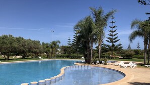 A swimming pool with a curved edge, surrounded by lounge chairs and palm trees. - APPT AT EDEN ISLAND BOUZNIKA WATERFRONT RESIDENCE (Bouznika)