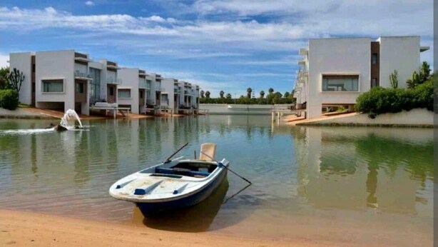 A modern building with a pool, a boat, and a chair. - APPT AT EDEN ISLAND BOUZNIKA WATERFRONT RESIDENCE (Bouznika)