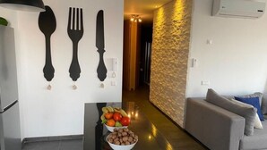 A modern kitchen with a dining area, a bowl of fruit, and a grey sofa. - APPT AT EDEN ISLAND BOUZNIKA WATERFRONT RESIDENCE (Bouznika)