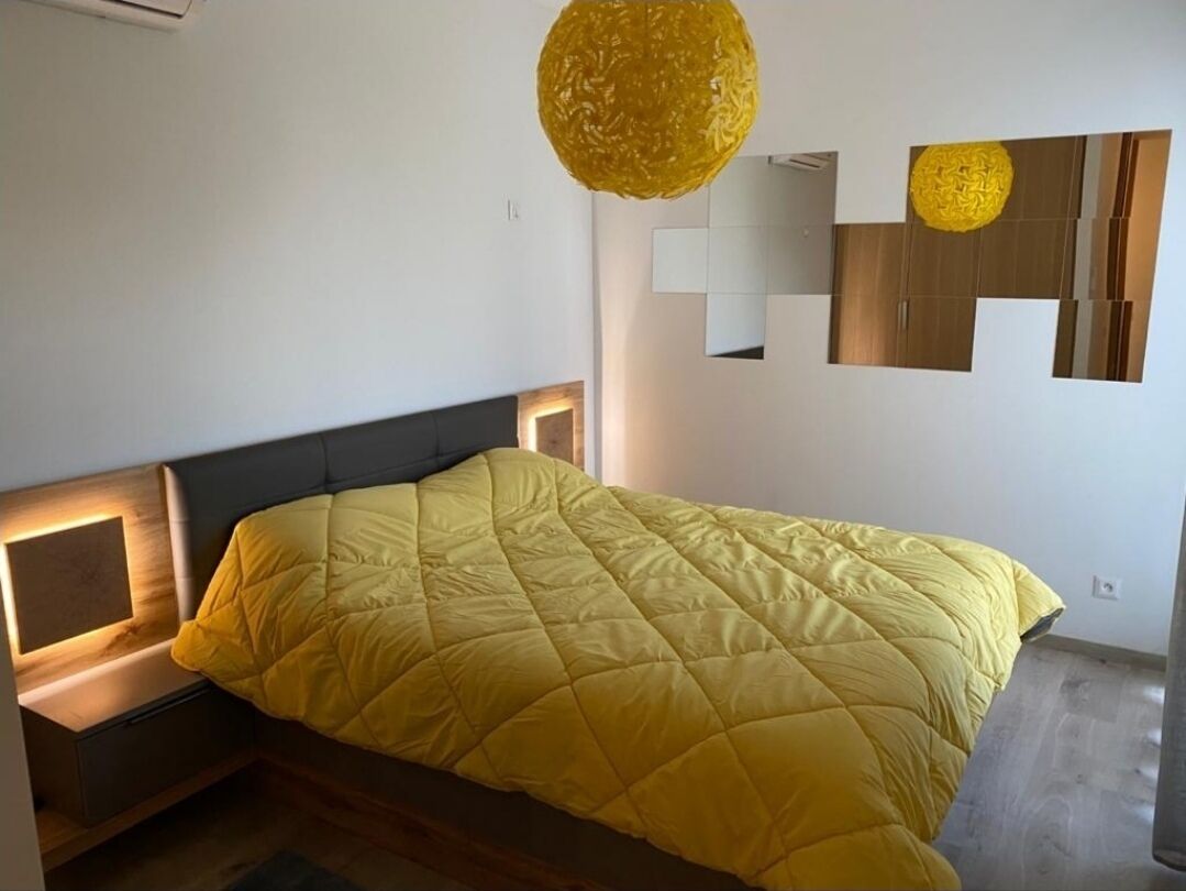 Una camera da letto moderna con un grande letto, un comodino, uno specchio fissato alla parete e un'originale lampada con texture.