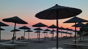 A beach with rows of sun loungers and thatched umbrellas, suggesting a beachside resort setting. - Sea View Luxury Villa (Siviri)