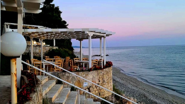 A seaside terrace with outdoor seating and a stone staircase leading to a beach. - Sea View Luxury Villa (Siviri)