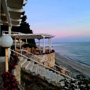 A seaside terrace with outdoor seating and a stone staircase leading to a beach. - Sea View Luxury Villa (Siviri)