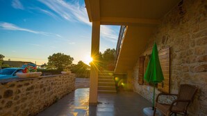 A stone-walled outdoor area with a staircase leading to an upper level, a wicker chair, and a green umbrella. - Steinhaus Punta Fuer 10 Personen-im Ortszentrum (Starigrad Paklenica)