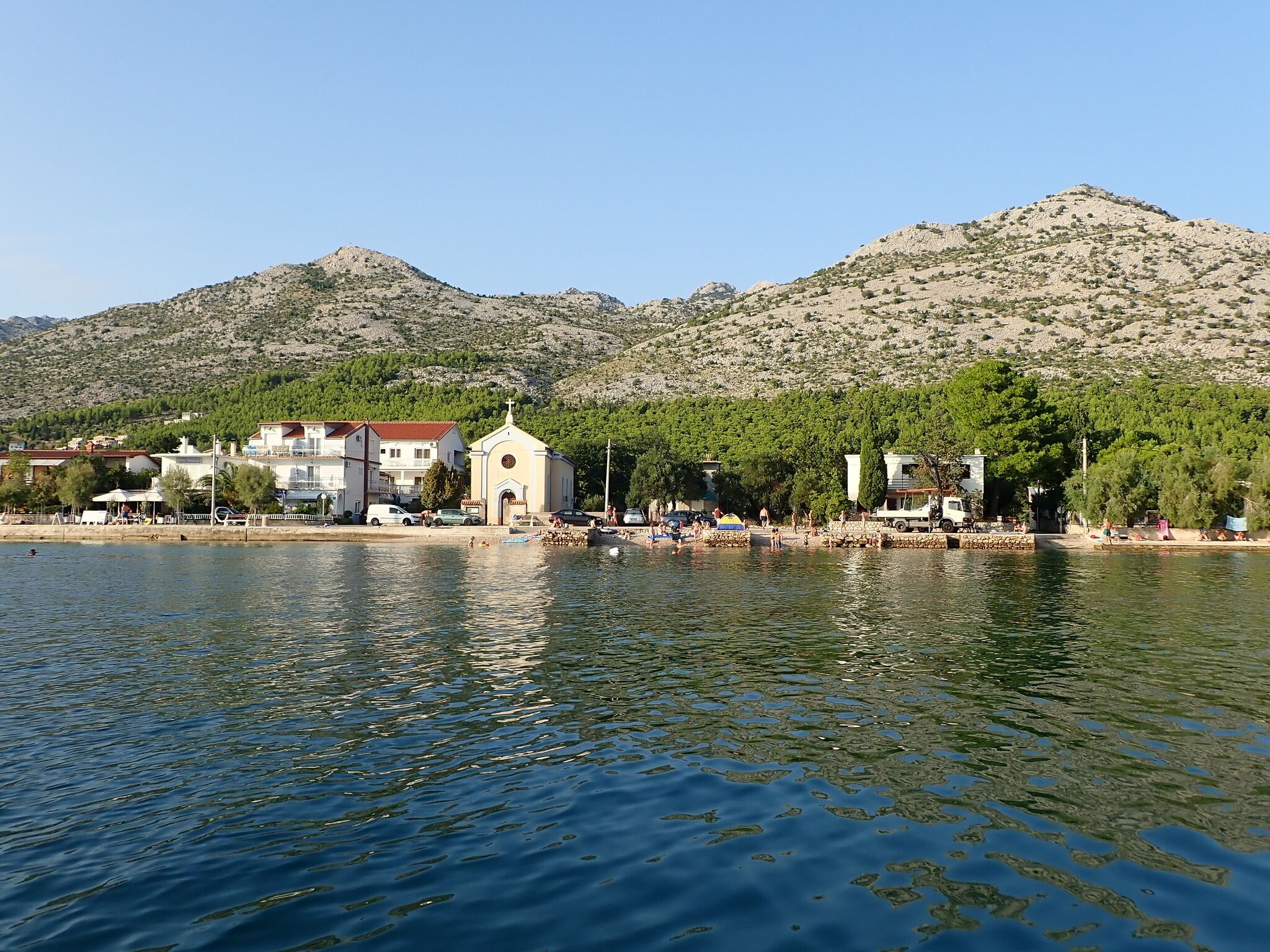 A coastal town with a church, buildings, and a mountain backdrop.