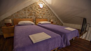 A bedroom with two beds, wooden floors, stone walls, and a sloped ceiling. - Steinhaus Punta Fuer 10 Personen-im Ortszentrum (Starigrad Paklenica)