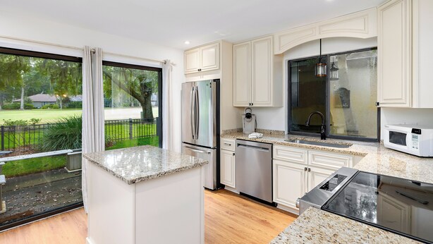 Una cocina moderna con armarios blancos, electrodomésticos de acero inoxidable y un amplio ventanal con vistas a un paisaje verde.