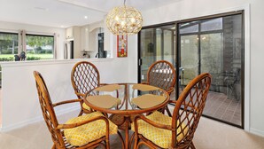Un comedor con una mesa redonda y cuatro sillas de mimbre con cojines amarillos, una lámpara colgante y un puerta corrediza de vidrio que da a un patio exterior.