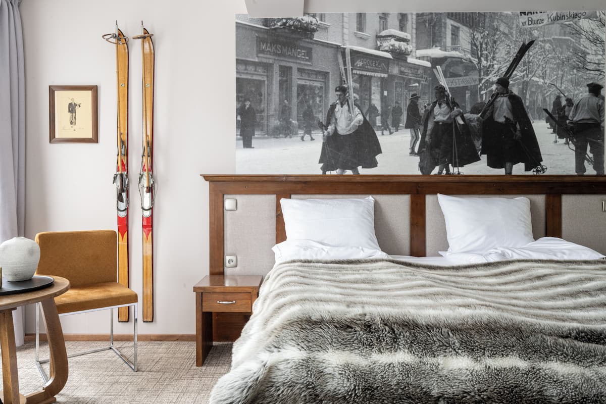 A hotel room with a bed, a chair, a nightstand, and a wall-mounted ski rack.